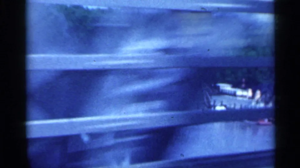 Motion-blurred 1959 Indiana bridge view shows river water, guardrail, wooded bank, and a small structure near the shore.