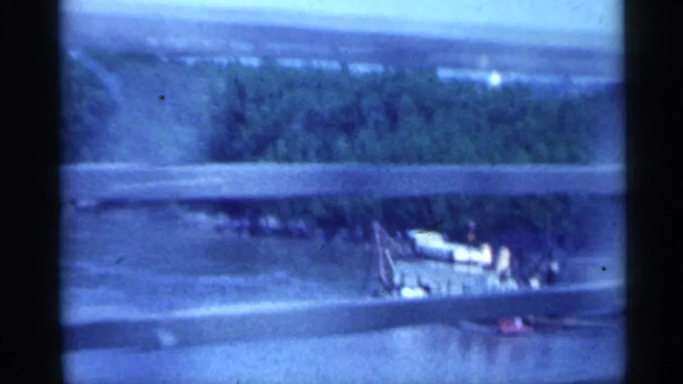 End of the 1959 Indiana bridge crossing view, showing guardrail, river water, trees, and a small riverside structure.