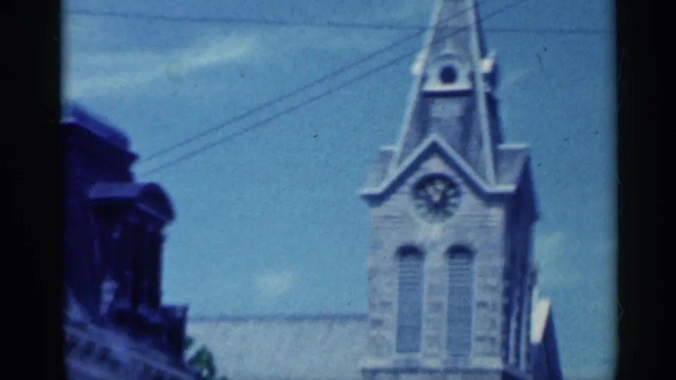 Soft 1959 Indiana 8mm frame showing a stone church clock tower partly obscured by the moving car interior.