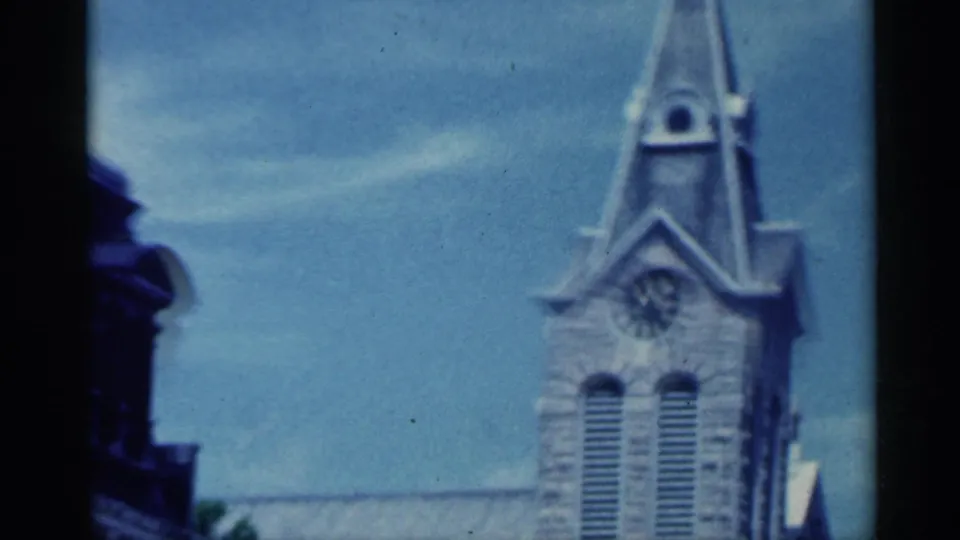 Indiana home-movie frame from 1959 showing the church steeple and clock tower in soft focus during a drive-by.