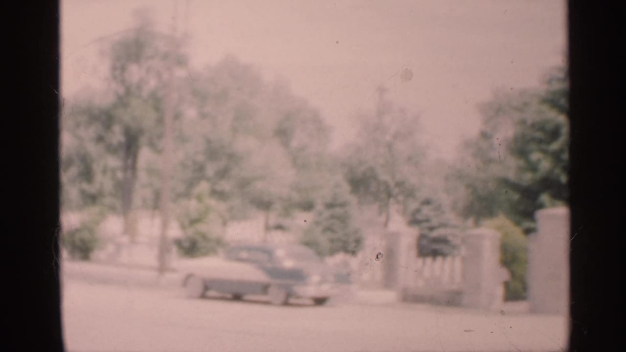 1959 Indiana road scene seen through a vehicle window, with a roadside car and trees softened by exposure and focus.