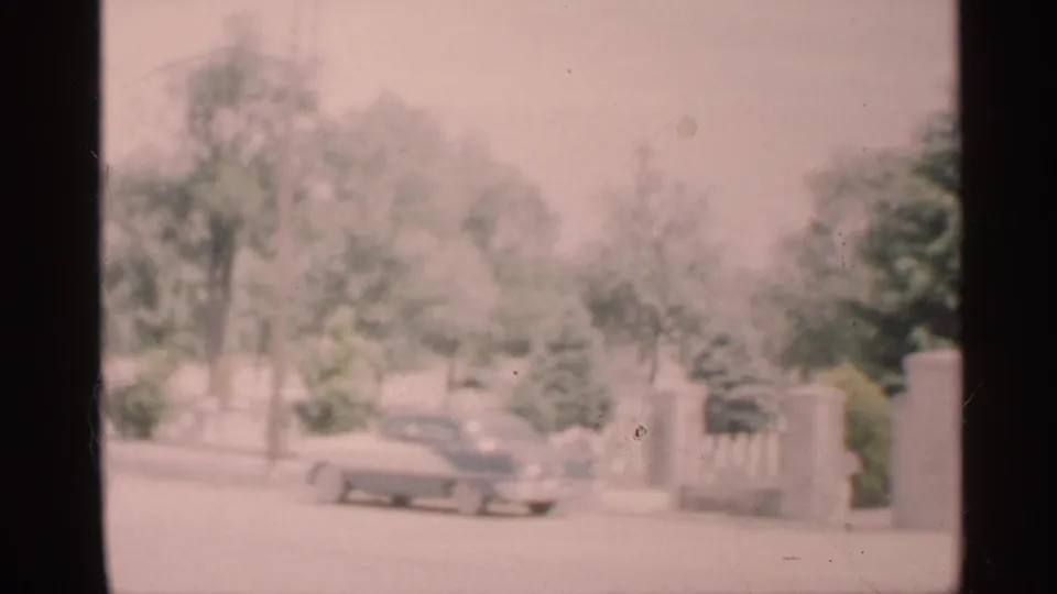 1959 Indiana road scene seen through a vehicle window, with a roadside car and trees softened by exposure and focus.