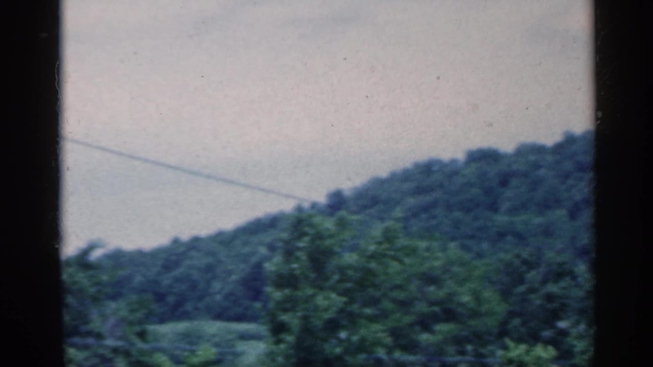 1959 Indiana 8mm frame showing green wooded hills, pale blue sky, and a faint utility line through dark film borders.