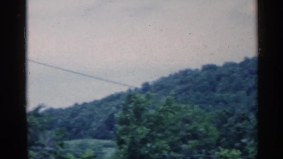 1959 Indiana 8mm frame showing green wooded hills, pale blue sky, and a faint utility line through dark film borders.