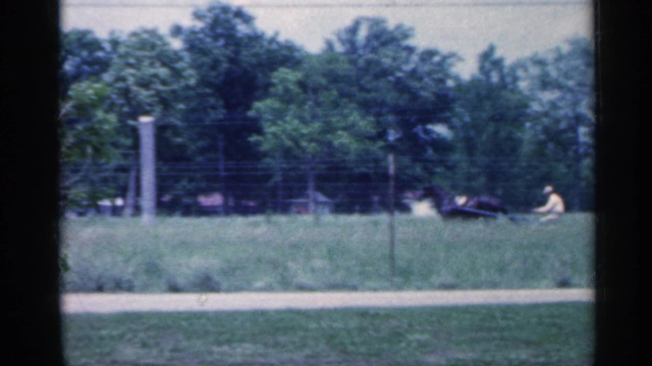 Horse and cart continue across a field with fence posts and trees behind them.