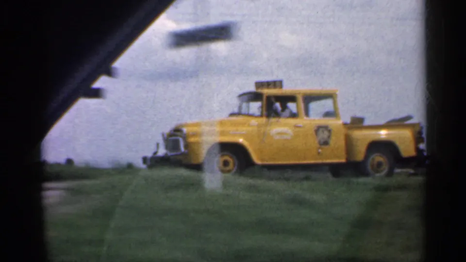 The yellow pickup is shown more clearly near the crossing sign, with vehicle markings visible but not reliably identifiable.