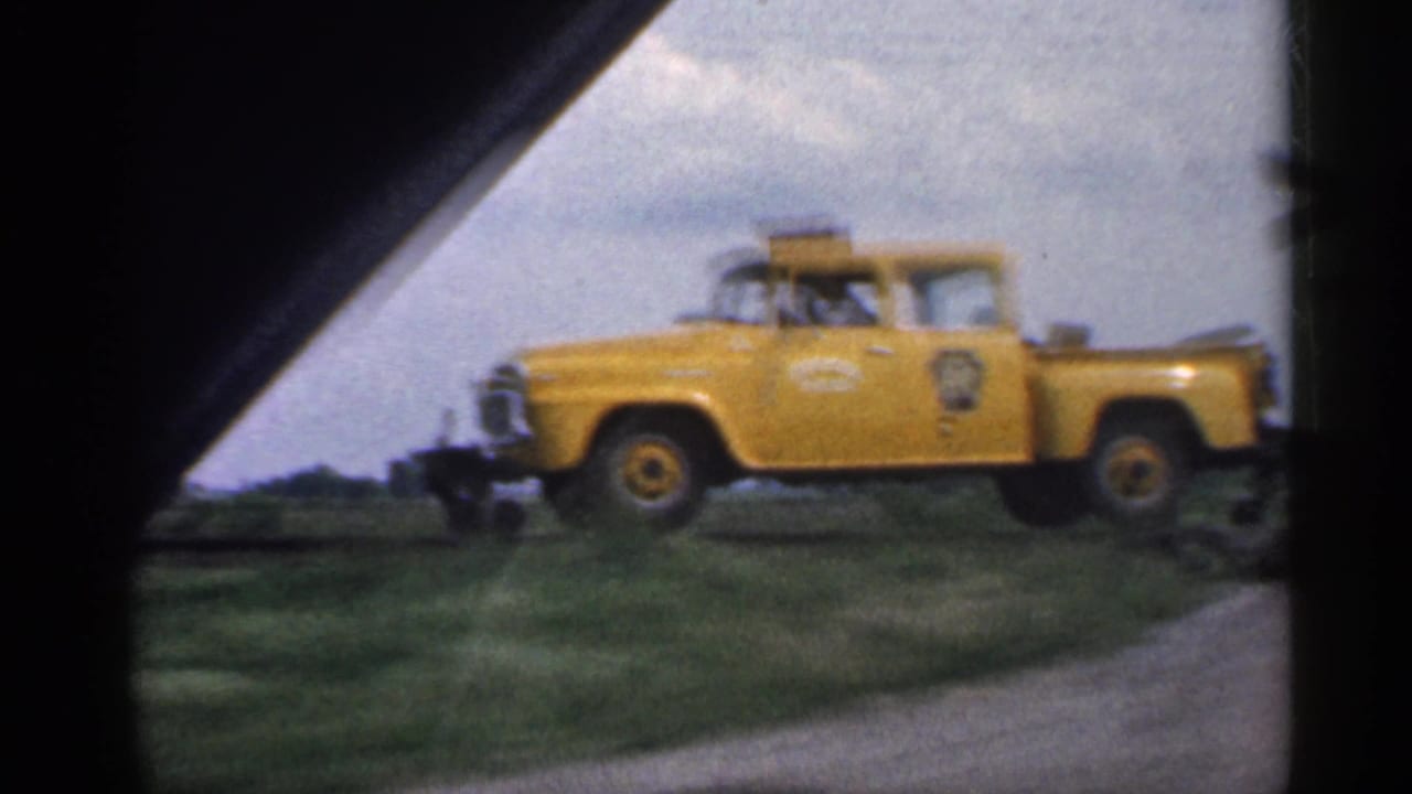 Yellow utility truck passing through a car-window view beside a rural road.
