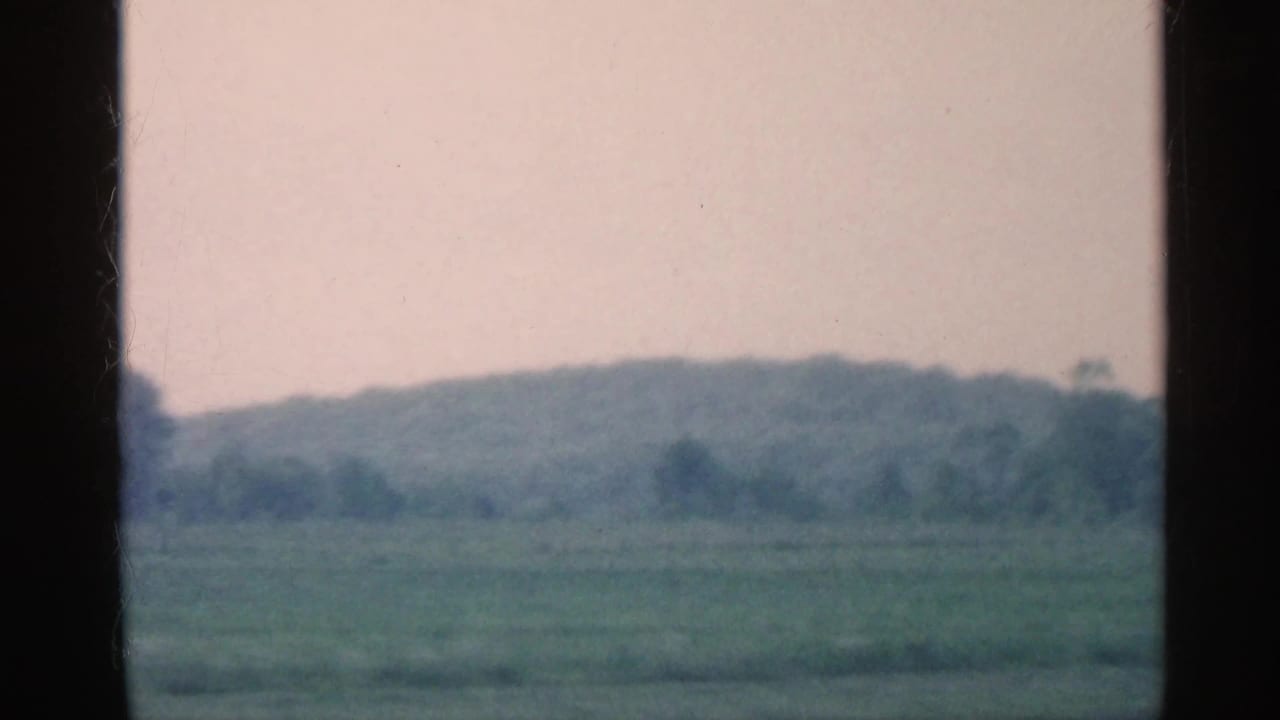 1959 Indiana 8mm frame showing hazy rural fields and a distant wooded ridge seen through the car window.