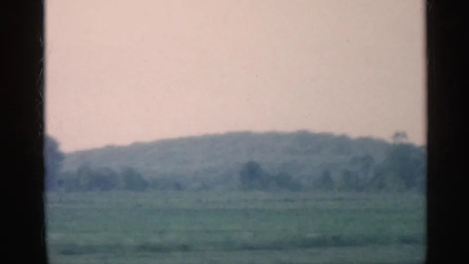 1959 Indiana 8mm frame showing hazy rural fields and a distant wooded ridge seen through the car window.