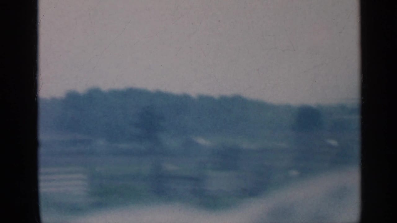 Soft 8mm view of Indiana countryside, with fields and distant trees partially obscured by motion blur and frame edges.