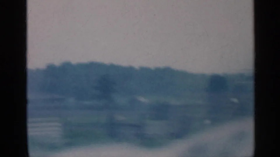 Soft 8mm view of Indiana countryside, with fields and distant trees partially obscured by motion blur and frame edges.