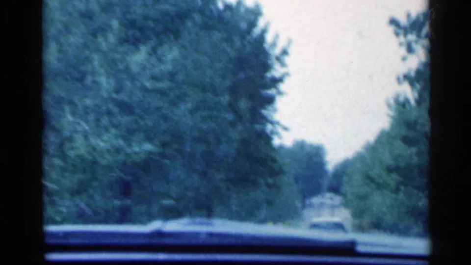 1959 Indiana 8mm windshield view of a wooded road with a distant car ahead.