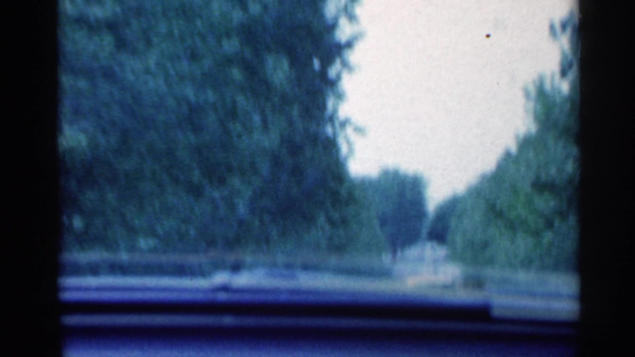 1959 Indiana home-movie view through a moving car windshield on a tree-lined road with dashboard visible.