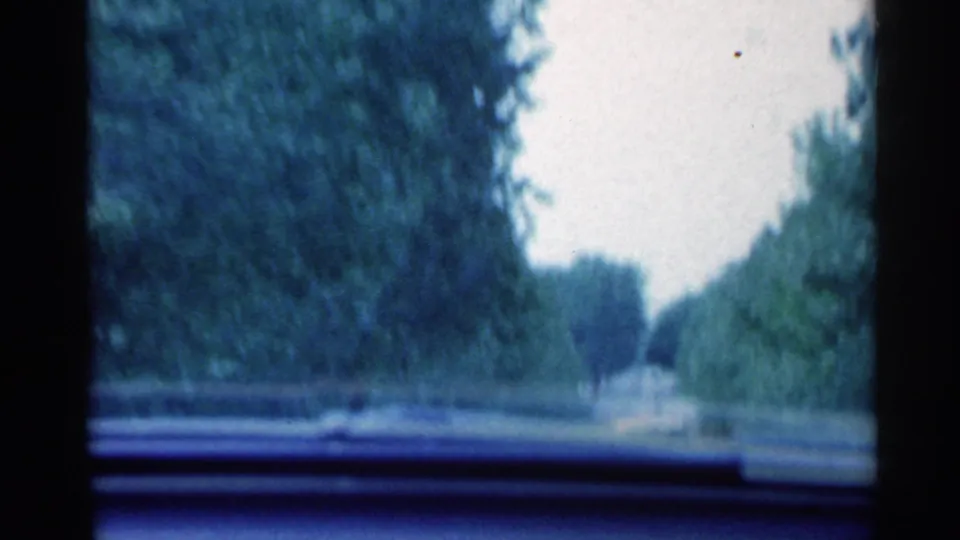 1959 Indiana home-movie view through a moving car windshield on a tree-lined road with dashboard visible.