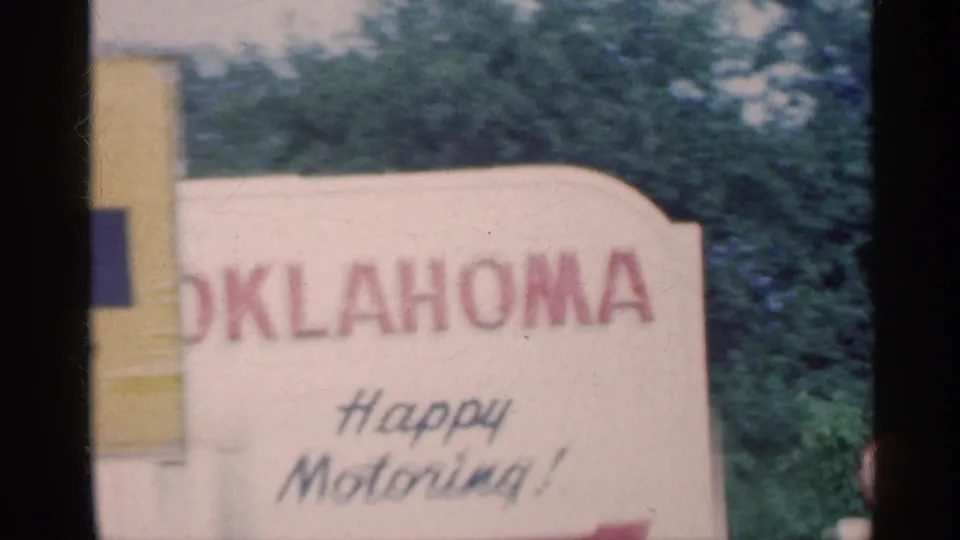 A roadside Oklahoma sign reading Happy Motoring is filmed from the moving car during the 1959 road trip.
