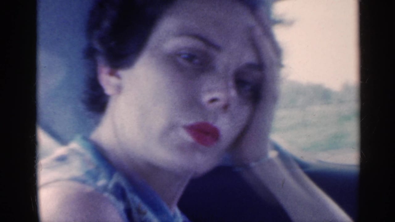 In this 1959 Indiana 8mm frame, a woman sits in a car and looks toward the camera while resting her head on her hand.