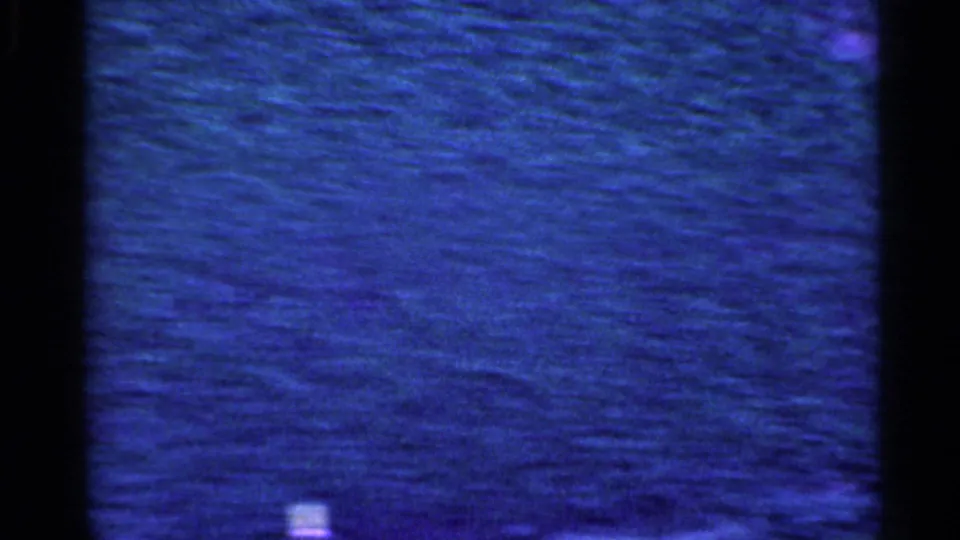 Blue-purple 8mm frame from inside a moving car in Indiana, showing a blurred roadside surface through dark window borders.