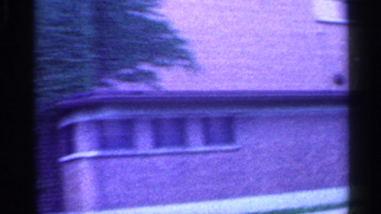 A soft, purple-tinted Indiana street-side structure passes outside the car window in this 1959 8mm home-movie frame.