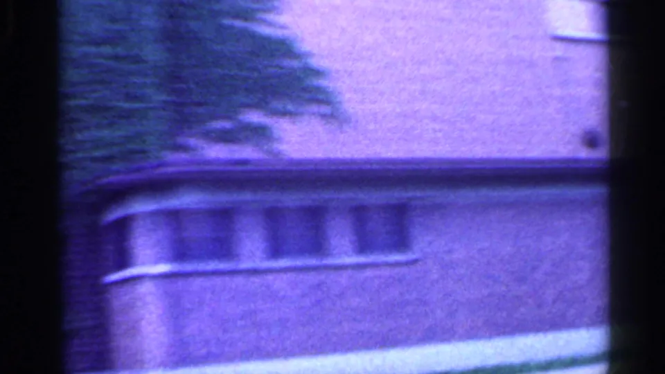 A soft, purple-tinted Indiana street-side structure passes outside the car window in this 1959 8mm home-movie frame.