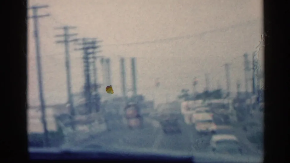 Forward-looking in-car view of an Indiana street in 1959, with utility poles, traffic, and parked or moving cars in soft focus.