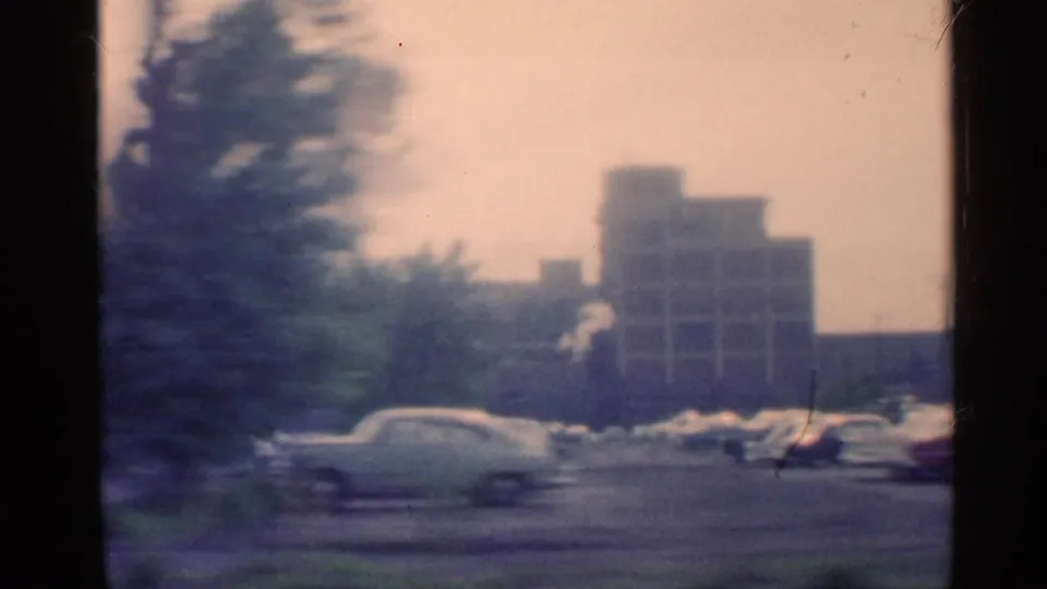 A tinted 1959 Indiana in-car street view shows automobiles, roadside trees, and a larger distant building in soft archival focus.