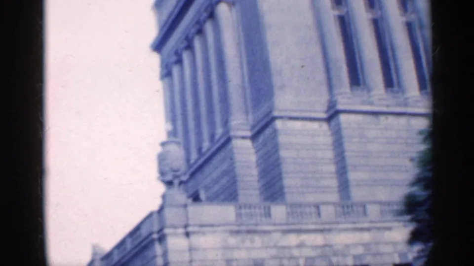 1959 Indiana frame showing a large masonry building facade with columns or pilasters beside a downtown street.