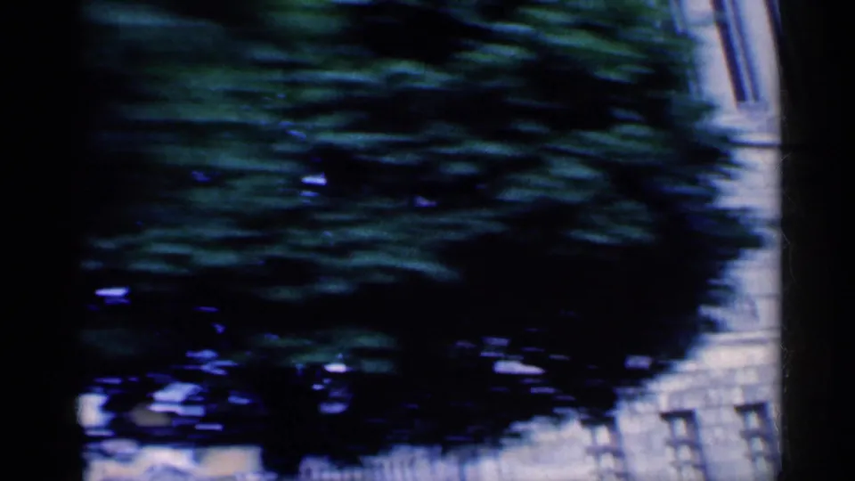1959 Indiana 8mm frame from inside a moving car, showing dark trees, a partial building, and window-frame shadows.