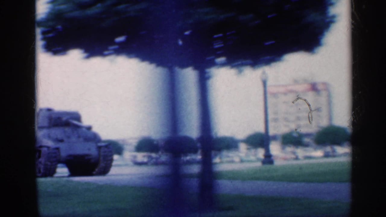Armored vehicle near grass, trees, and a distant monument.