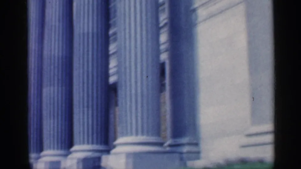 Close 1959 Indiana 8mm view of tall classical columns, column bases, pale stone wall, and slight handheld blur.