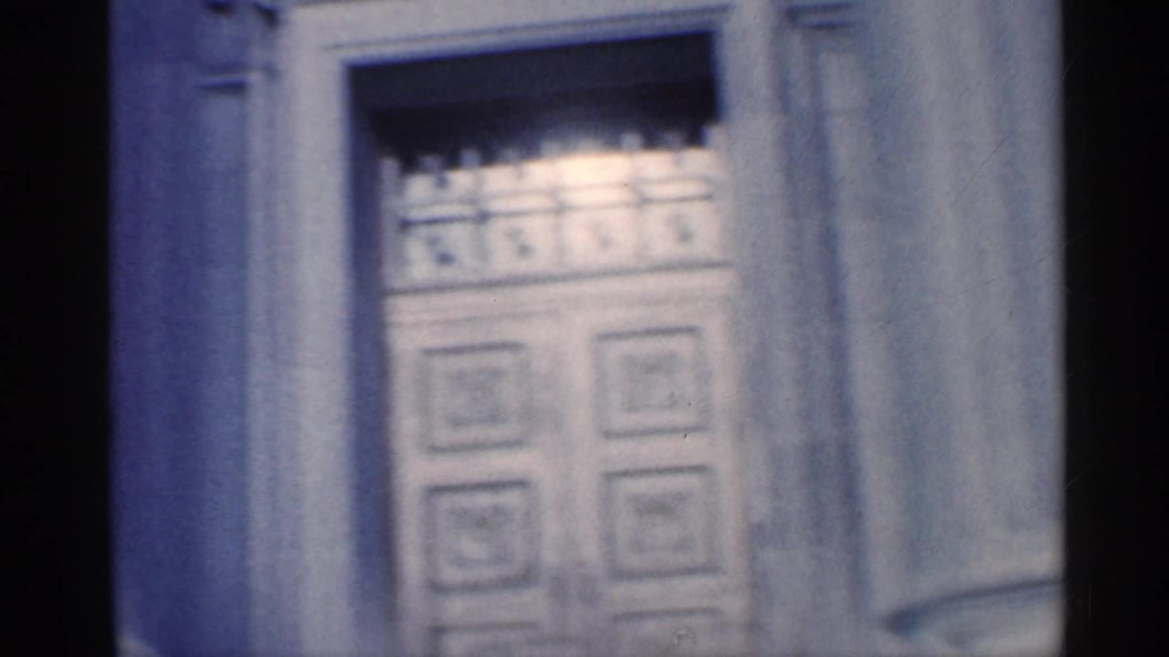 Soft close view of a classical column and ornate doorway on a stone building.