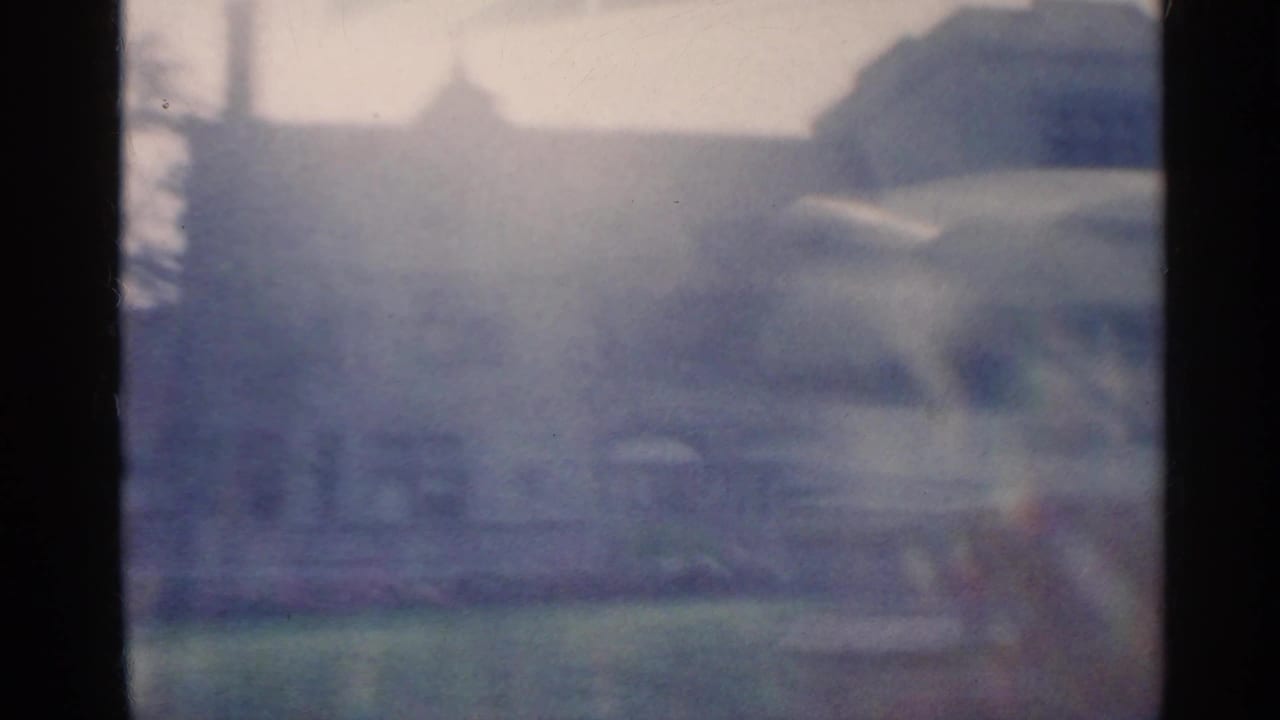 Hazy view from a moving car toward a large building and lawn.