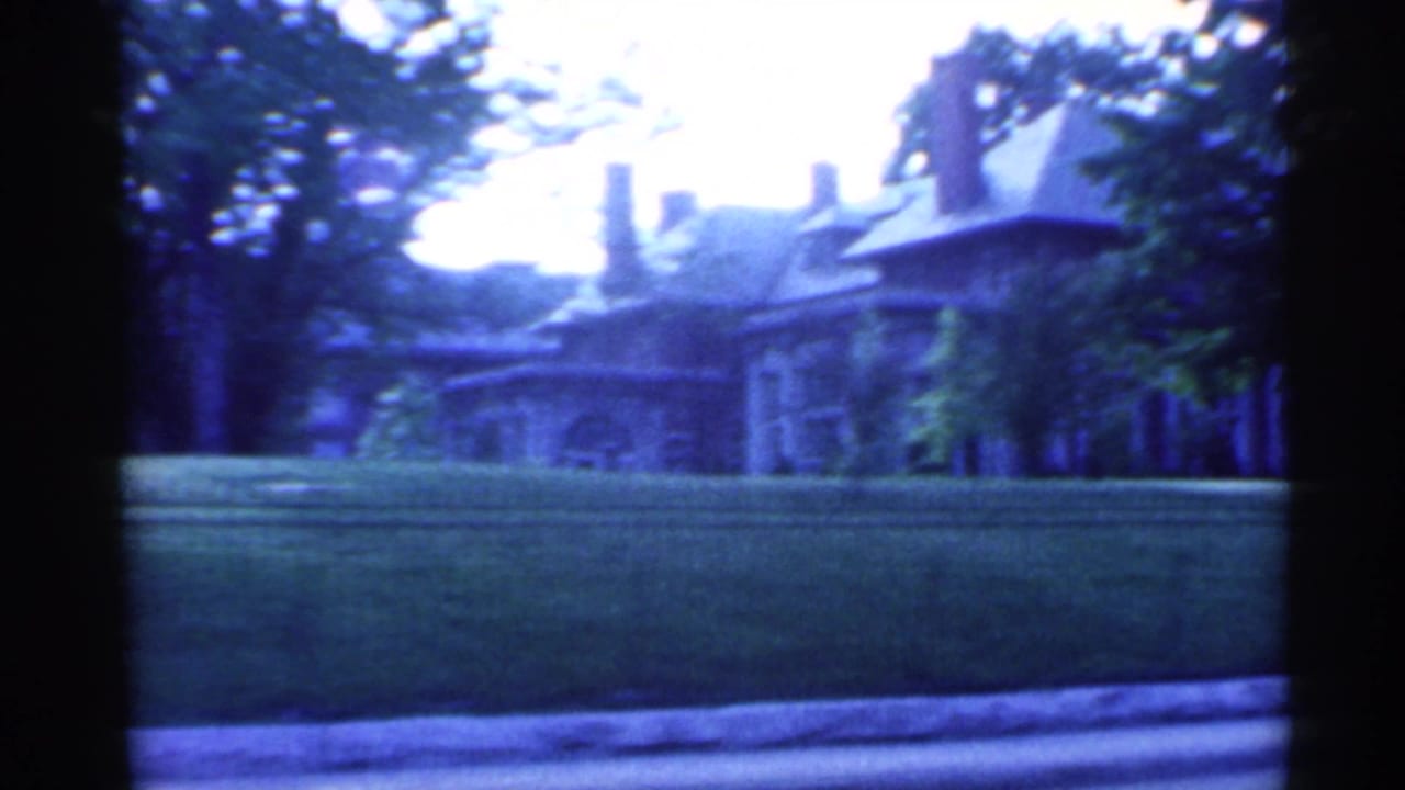 1959 Indiana 8mm frame showing a large residential building behind a manicured lawn, low iron fence, and mature trees.
