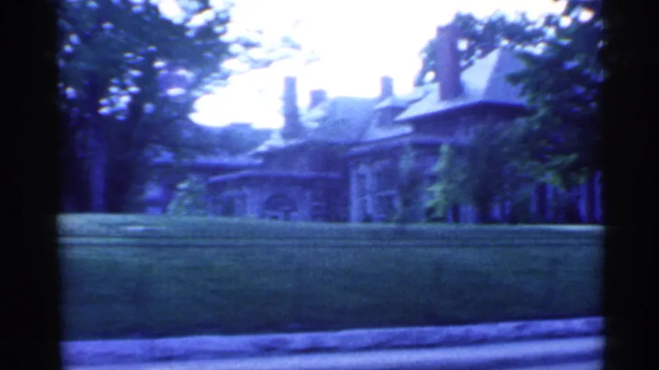 1959 Indiana 8mm frame showing a large residential building behind a manicured lawn, low iron fence, and mature trees.