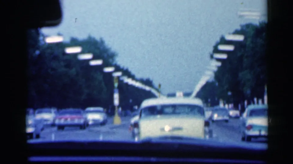 Final 1959 Indiana road frame shows cars moving ahead beneath rows of streetlights, with the car interior framing the lower edge.