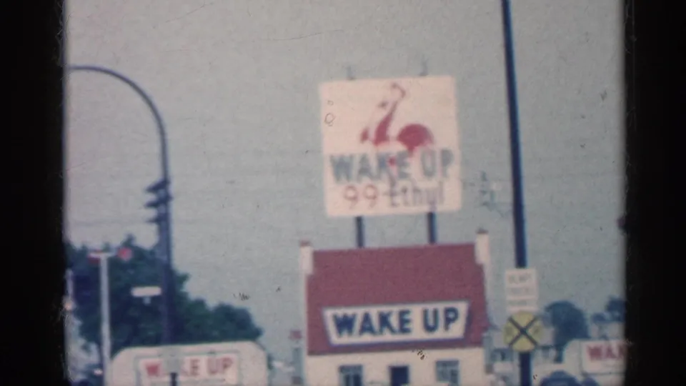 Indiana roadside view with a Wake Up 99 Ethyl sign, traffic signal, utility poles, and windshield framing from the moving car.