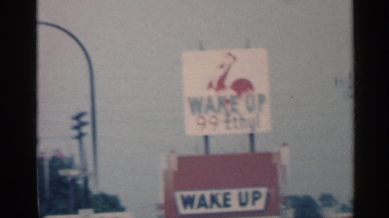 Red and white Wake Up 99 Ethyl sign beside a roadside with utility poles.
