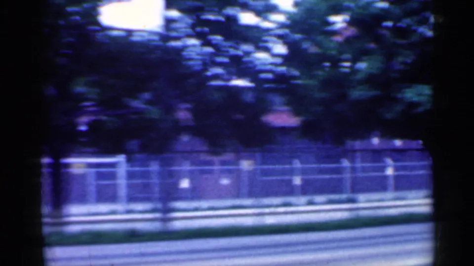 Trees, fencing, and a roadside verge pass by in the final 1959 Indiana frame, softened by home-movie motion blur.