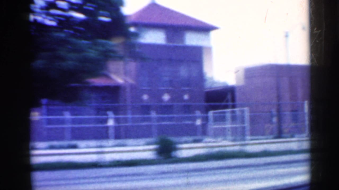 Brick building behind chain-link fence seen from a moving vehicle.