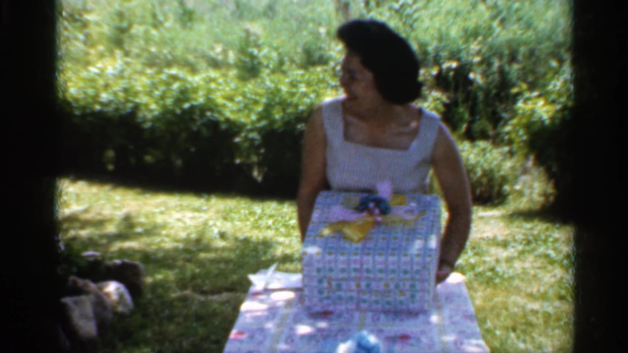Woman turns toward the side while holding a wrapped gift on the table.