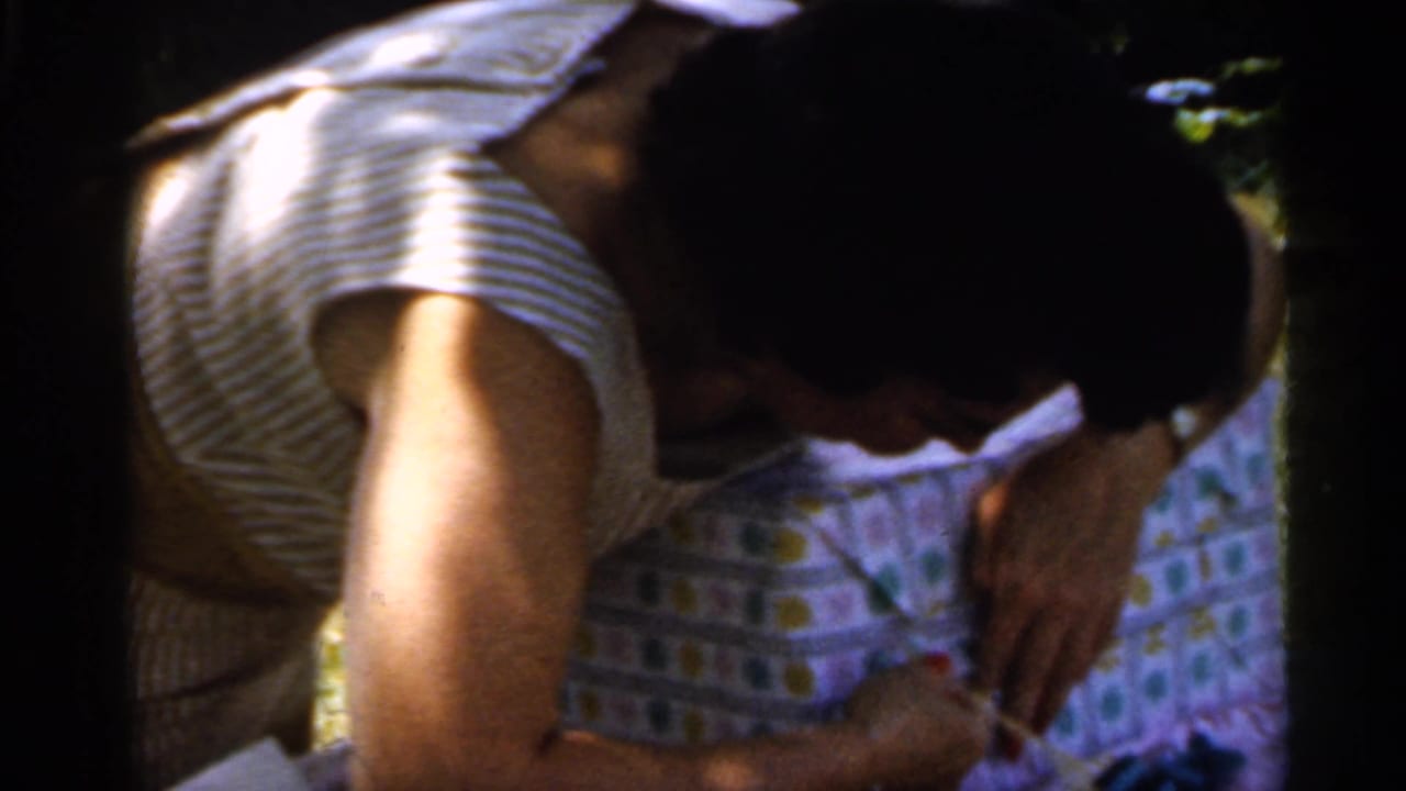 Woman bends over a wrapped present on a shaded lawn.