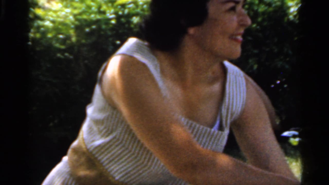 The woman sits on a grassy lawn in Indiana, smiling to the side while wearing a white striped sleeveless top.