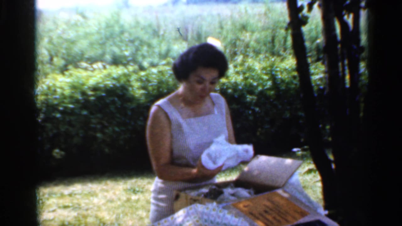 Woman in a white sleeveless dress unwraps tissue from a box on an outdoor table.
