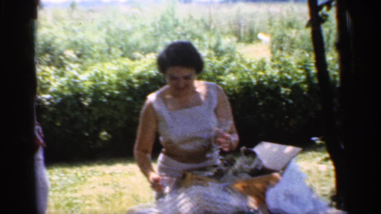 Woman in a white sleeveless dress sits outdoors with gifts on a sunny lawn.