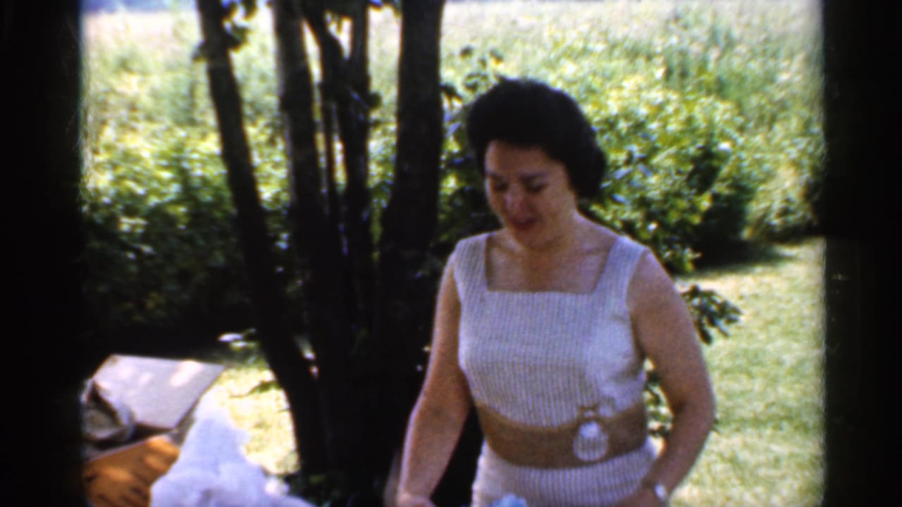 Woman in a striped dress stands by an outdoor table in a shaded garden.
