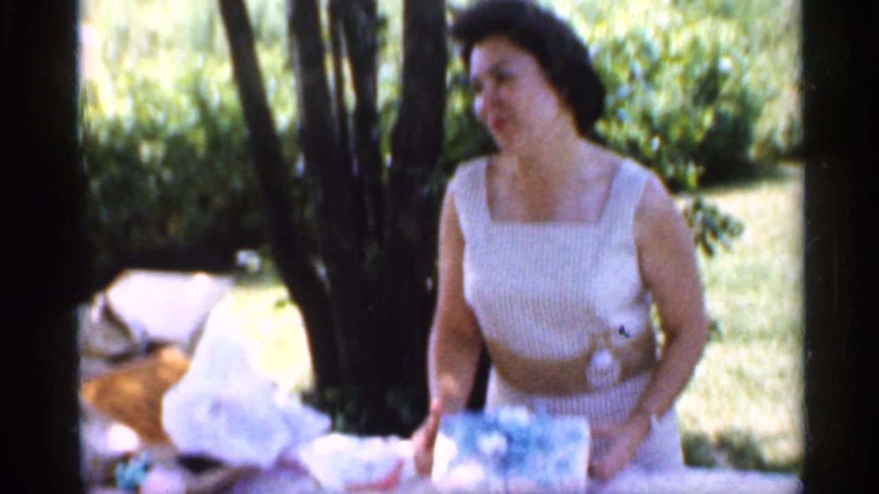 A woman in a white striped dress smiles while handling gift wrapping at an outdoor table in Indiana, 1959.
