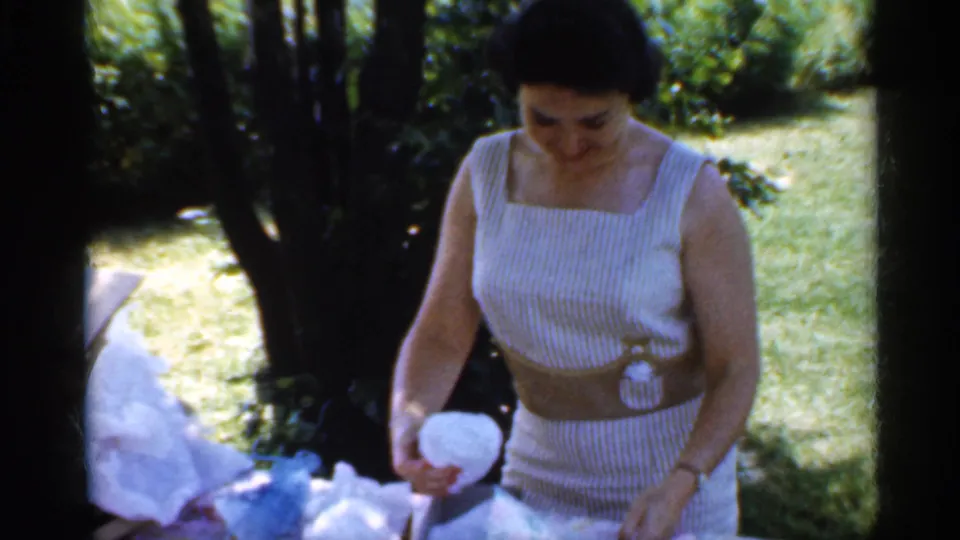 In the final frame, the woman holds a white round object or bundled wrapping near the picnic table, with shaded trees and lawn behind her.