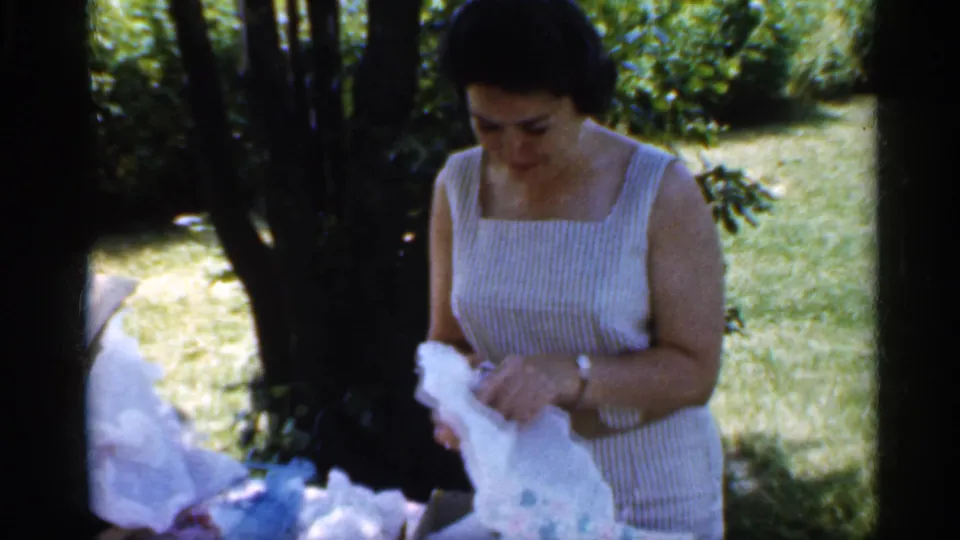 A woman looks down with focused attention as she continues opening a gift in a leafy Indiana garden setting.