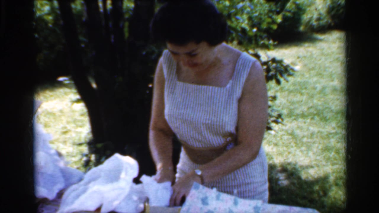 Woman looks down at tissue paper and a wrapped package beside trees and grass.