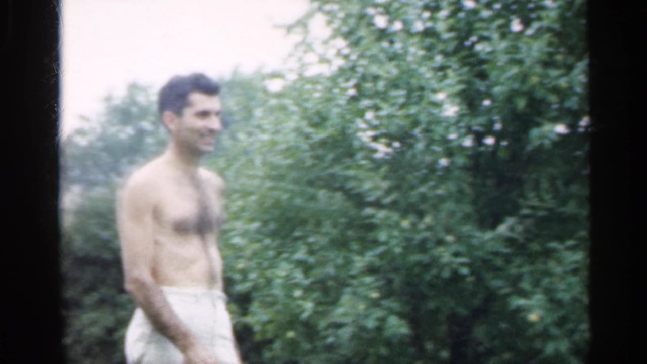 Shirtless man in light shorts smiling in a green backyard.