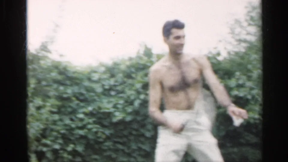 A shirtless man in white shorts holds a badminton racket in the supplied 1959 Indiana 8mm backyard recreation footage.